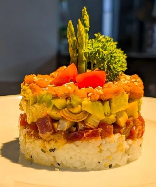Elegant layered sushi tartare made with fresh salmon, tuna, avocado, and rice, garnished with cherry tomatoes, asparagus, and parsley.