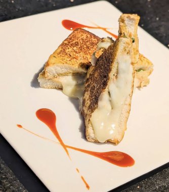 Closeup of a grilled cheese sandwich filled with melted mozzarella cheese, served on a white plate with artistic red sauce decoration.
