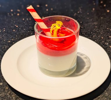 A beautifully layered Italian-style panna cotta or pudding dessert, featuring a creamy white base and a bright red fruit sauce.