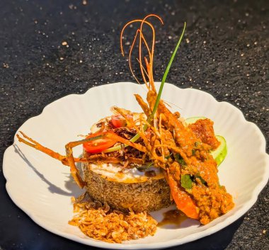 Elegant plating of savory fried rice topped with a whole river prawn (or lobster/large shrimp) coated in a thick, spicy curry sauce, garnished with cherry tomatoes, a fried egg, and crispy shallots.