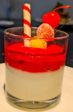 A beautifully layered Italian-style panna cotta or pudding dessert, featuring a creamy white base and a bright red fruit sauce.