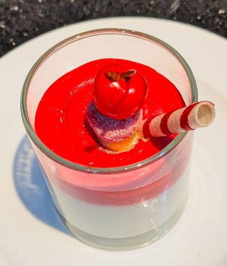 A beautifully layered Italian-style panna cotta or pudding dessert, featuring a creamy white base and a bright red fruit sauce.