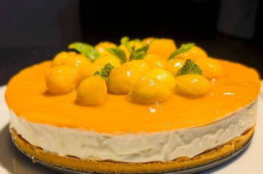 Elegant mango cheesecake topped with glossy melon balls and mint leaves, showcasing a vibrant tropical dessert.