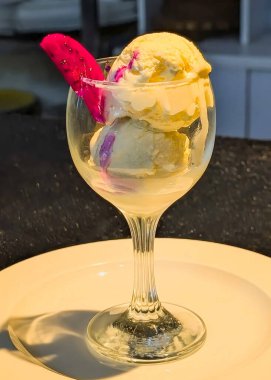 Zarif bir bardakta sunulan vanilyalı dondurma üzerine bir dilim ejderha meyvesi serpilmiş ve yoğun süt serpilmiş..