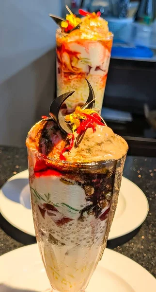 Delicious chocolate sundae served in a tall glass with layers of ice cream, chocolate syrup, nuts, and cherry topping.