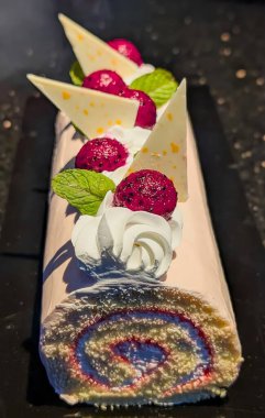 Krem şanti, beyaz çikolata parçaları ve taze nane yapraklarıyla süslenmiş zarif yusufçuk meyveli İsviçre pastası..