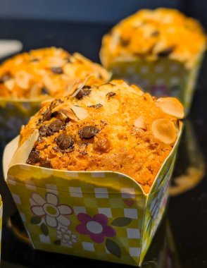 Badem dilimleriyle kaplı yeni pişmiş çikolatalı kekin yakın çekimi, sıcak ışığın altında dekoratif bir kağıt bardakta sunuluyor..