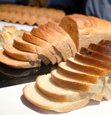 Ilık ışığın altında tezgahın üzerinde düzgünce dilimlenmiş beyaz ekmek somunu. Yumuşak, yumuşak dokusu ve altın kabuğu onu fırın promosyonları için ideal kılıyor.