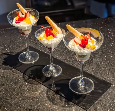 Üç zarif parfe ustaca çırpılmış krema, taze meyve ve şeffaf martini bardaklarında servis edilen çıtır çıtır bisküvi ile kaplı..