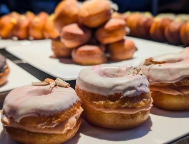Beyaz badem jöleli ve pembe kıvrımlı, yumuşak kremayla dolu ve beyaz bir tabakta servis edilen taze pişmiş donut sıraları..