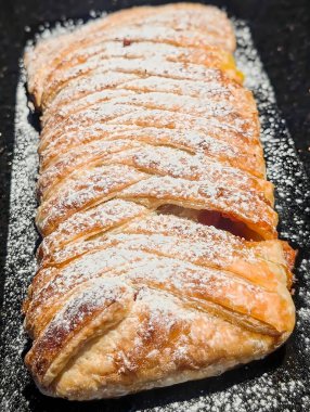 Bir yığın pullu, altın-kahverengi puf böreği, ya da samosa, zıt bir koyu granit yüzeye karşı uzun beyaz bir dikdörtgen tabakta sunulur..