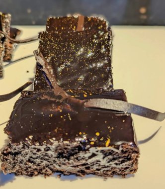 Üstü karamel kıvrımlı çikolatalı brovniler ve parlak siyah çikolata serpiştirilmiş zarif beyaz bir tabakta zarif çikolata garnitürle sunulmuş..