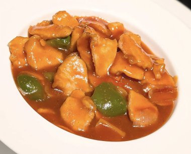 Yeşil dolmalık biberli ve soğanlı portakal soslu taze tavuk parçaları içeren tatlı ve ekşi tavuğun yakın çekimi..