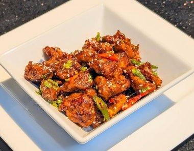 Parlak baharatlı sosun içine susam, acı biber ve bitkiler karıştırılmış kızarmış tavuk parçaları..