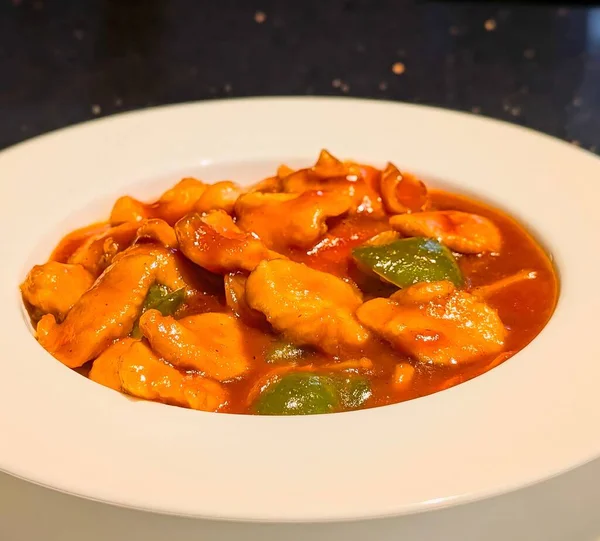 Yeşil dolmalık biberli ve soğanlı portakal soslu taze tavuk parçaları içeren tatlı ve ekşi tavuğun yakın çekimi..