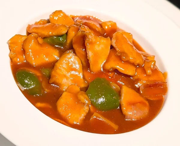 Yeşil dolmalık biberli ve soğanlı portakal soslu taze tavuk parçaları içeren tatlı ve ekşi tavuğun yakın çekimi..