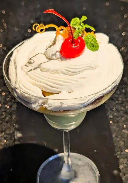 Parlak kırmızı kiraz, nane yaprakları ve karamel süsleme ile kaplı bir bardakta servis edilen zarif krem şantili tatlı..