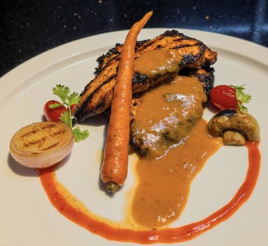 Zengin, kadife turuncu-kahverengi bir sosla kaplanmış ızgara ızgara izleri ve nemli bir dokuyla ustalıkla pişirilmiş, görsel olarak çarpıcı bir tabak..