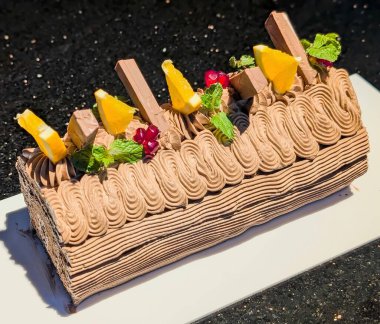 Kalın borulu çikolatalı kremayla kaplı yoğun bir çikolatalı pasta. Ağaç kabuğuna benzeyen, zengin ve yoğun bir dokuyu vurguluyor..