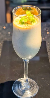 Serinletici tatlı Lassi zarif cam takımla servis ediliyor, ezilmiş fındık ve nane yapraklarıyla kaplı..