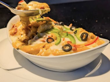 Dinamik yakın plan, bir kaşık kremalı, fırınlanmış makarna beyaz oval kaseden kaldırılıyor, yapışkan, erimiş peynir ve lezzetli sosu vurguluyor..