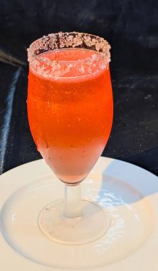 Şekerle kaplı soğuk bir bardakta servis edilen pırıl pırıl kırmızı bir moktail..