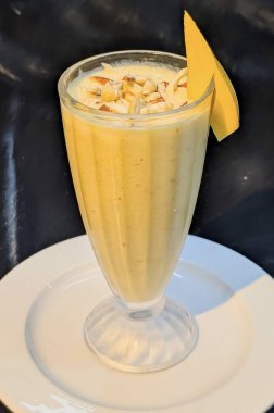 Zengin ve kremalı bir mango milkshake, üzerine doğranmış fındık ve mango dilimi ile süslenmiş..