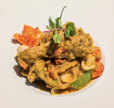 Beyaz bir tabakta servis edilen iki lezzetli but ve canlı kırmızı biber ve taze nane ile süslenmiş zengin, kahverengi körili tavuk sunumu..