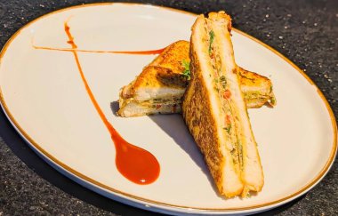 Çaprazlama dilimlenmiş, altın renginde, tuzlu bir sandviçin profesyonel pozu, kalın bir yumurta, sebze ve şifalı bitkiyi ortaya çıkarmak için, ince bir altın kenarlı beyaz tabak sunuldu..