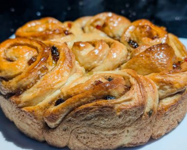 Beyaz bir tabakta sergilenen altın sarısı, jöleli tarçınlı kuru üzümlü ekmek, zengin girdaplarını, yumuşak dokusunu ve mükemmel pişmiş kabuğunu vurguluyor..