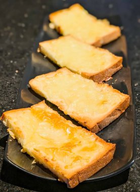 Pürüzsüz siyah bir tabakta servis edilen gevrek peynirli sarımsaklı ekmek, erimiş peynir ve kızarmış altın dokuma..