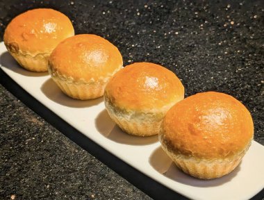 Dar beyaz servis tabağında mükemmel hizalanmış, taze pişmiş, altın sarısı çörekler veya tatlı çöreklerden oluşan dikey bir yakın çekim..