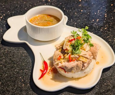 Profesyonel bir stüdyo çekiminde taze haşlanmış tavuk ya da buğulanmış tavuk, dilimlenmiş ve güzel kokulu pirinç kubbesi üzerinde servis edilmiş, eşsiz, yaprak şeklinde beyaz seramik bir tabakta güzelce kaplanmış.