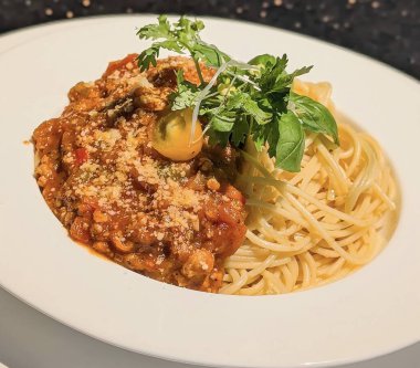 Cömert bir spagetti servisi zengin, lezzetli bir bolonez et sosuyla kaplanır, rendelenmiş parmesan peyniri ile tozlanır, ve zarif bir şekilde taze mikroçerez ve fesleğenle süslenir..