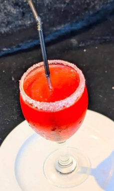 Coşkulu kırmızı bir mocktail soğuk bir kadehte sunuluyor kaba bir şeker çemberi ve pipet, parlak renkler ve ferahlatıcı dokular sergiliyor..