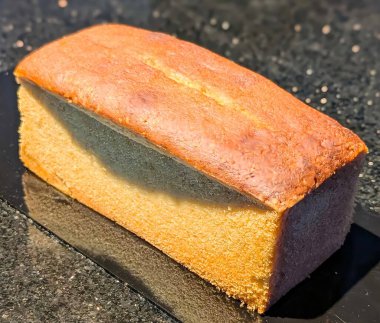 Altın kabuklu, yumuşak, ince kırıntılı taze pişmiş vanilyalı kek. Temiz ve ticari bir görünüm için koyu renkli bir yansıtıcı yüzeyde sergileniyor..