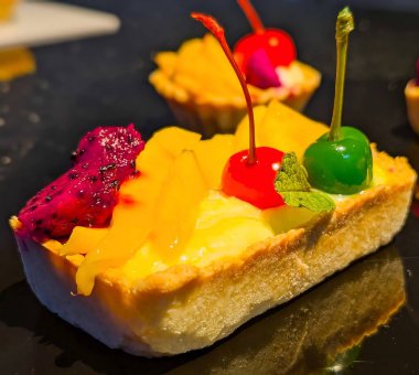 Dikdörtgen şeklinde, tereyağlı kabuklu, kremalı ve canlı mango dilimleri ve mor ejderha meyvelerinden oluşan tropikal meyveli turtanın yakın çekimi..