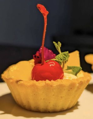 Taze mango, mor ejderha meyvesi ve parlak yeşil maraschino vişneli kremalı kremalı kremalı hamur tatlısı içeren canlı mini meyveli turtalar.