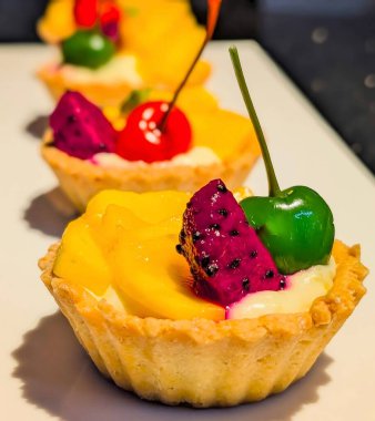 Taze mango, mor ejderha meyvesi ve parlak yeşil maraschino vişneli kremalı kremalı kremalı hamur tatlısı içeren canlı mini meyveli turtalar.