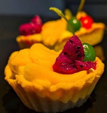 Taze mango, mor ejderha meyvesi ve parlak yeşil maraschino vişneli kremalı kremalı kremalı hamur tatlısı içeren canlı mini meyveli turtalar.