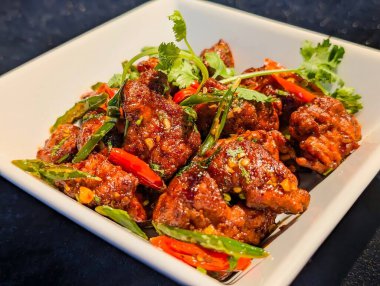 Yakın plan, kıtır kıtır Asya biberli tavuk parçaları, içine tuzlu, tatlı bir sos atılmış ve taze kişniş, kırmızı ve yeşil kırmızı biberlerle süslenmiş..