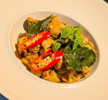 Taze Tayland fesleğeni ve dilimlenmiş kırmızı biberle süslenmiş, bol baharatlı tavuk, soğan ve köri yapraklarından oluşan otantik Tayland usulü kızartma..