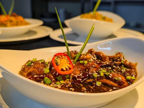 Lezzetli Mançurya tavuk parçalarının yakın plan çekimi zengin, koyu jöleli, kızarmış susam tohumu, doğranmış soğan ve bir dilim kırmızı biber ile süslenmiş..