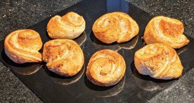 Lezzetli bir şekilde pişirilmiş, altın sarısı tarçınlı börekler, tatlı dolgu ve yumuşak hamur işleri içeren, cilalı siyah bir levhada veya taş bir yüzeyde güzelce sunulan.