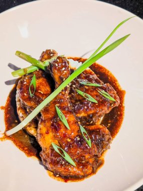 Taze yeşil soğan ve susam tohumları ile süslenmiş, yoğun bir şekilde yapışkan, parlak teriyaki tarzı bir jöle ile kaplanmış lezzetli bir protein sunumu.