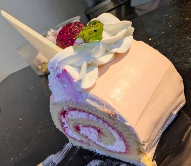 Pembe şekerleme, krema sarmalı ve canlı ejderha meyveli pastadan oluşan güzel bir İsviçre pastası. Krem şanti, nane yaprağı ve siyah bir yüzeyde beyaz çikolata parçalarıyla kaplı..