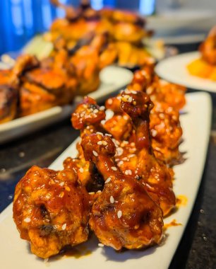 Parlak kırmızımsı turuncu bir jöle ile kaplanmış, beyaz susam tohumlarıyla süslenmiş ve beyaz dikdörtgen bir tabakta düzgünce sıralanmış tavuk eti..