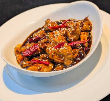 Kurutulmuş kırmızı biber ve susam tohumlarıyla süslenmiş, soya bazlı zengin bir jöleli taze tavuk parçaları içeren cesur bir Kung Pao tavuğu..