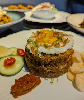 Lezzetli bir kızarmış pilav servisinin üstü kızarmış yumurta, kıtır ançüez, taze soğan ve temiz beyaz bir tabakta sunulan taze limon dilimi ile kaplıdır..