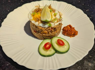 Lezzetli bir kızarmış pilav servisinin üstü kızarmış yumurta, kıtır ançüez, taze soğan ve temiz beyaz bir tabakta sunulan taze limon dilimi ile kaplıdır..